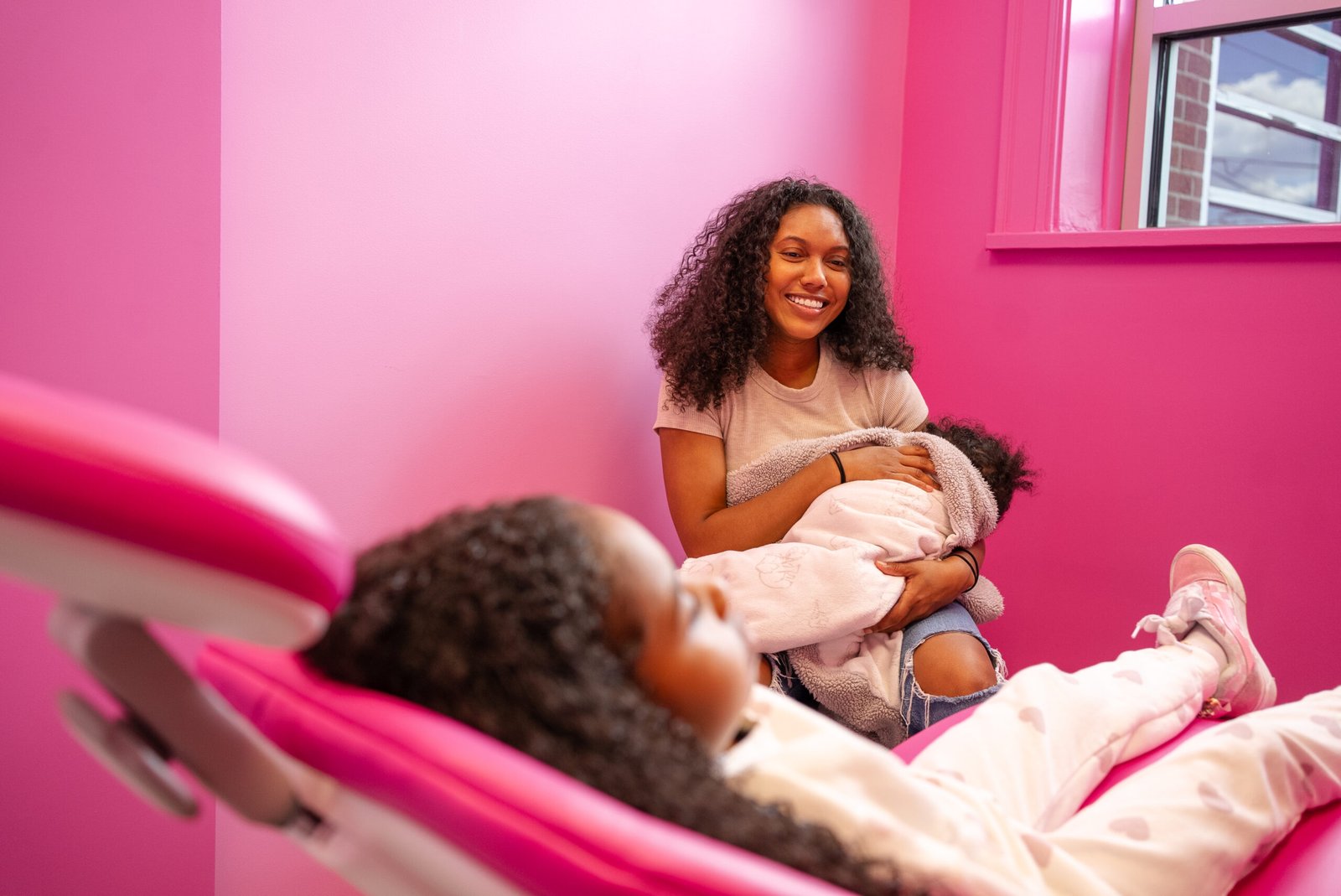 Woman relaxing on couch holding her baby against pink background, conveying comfort, ease, and modern lifestyle.