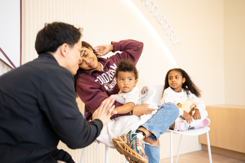 Dentist sitting with family and children together, smiling and interacting in friendly pediatric dental office setting.