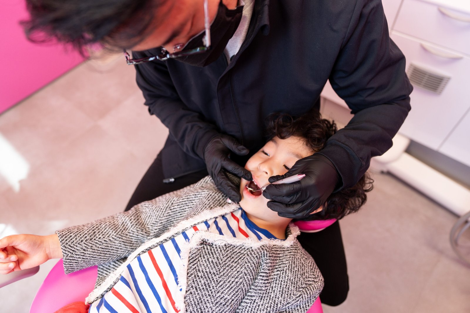 Dentist examining child lying in dental chair, using tools carefully during pediatric dental treatment procedure session.