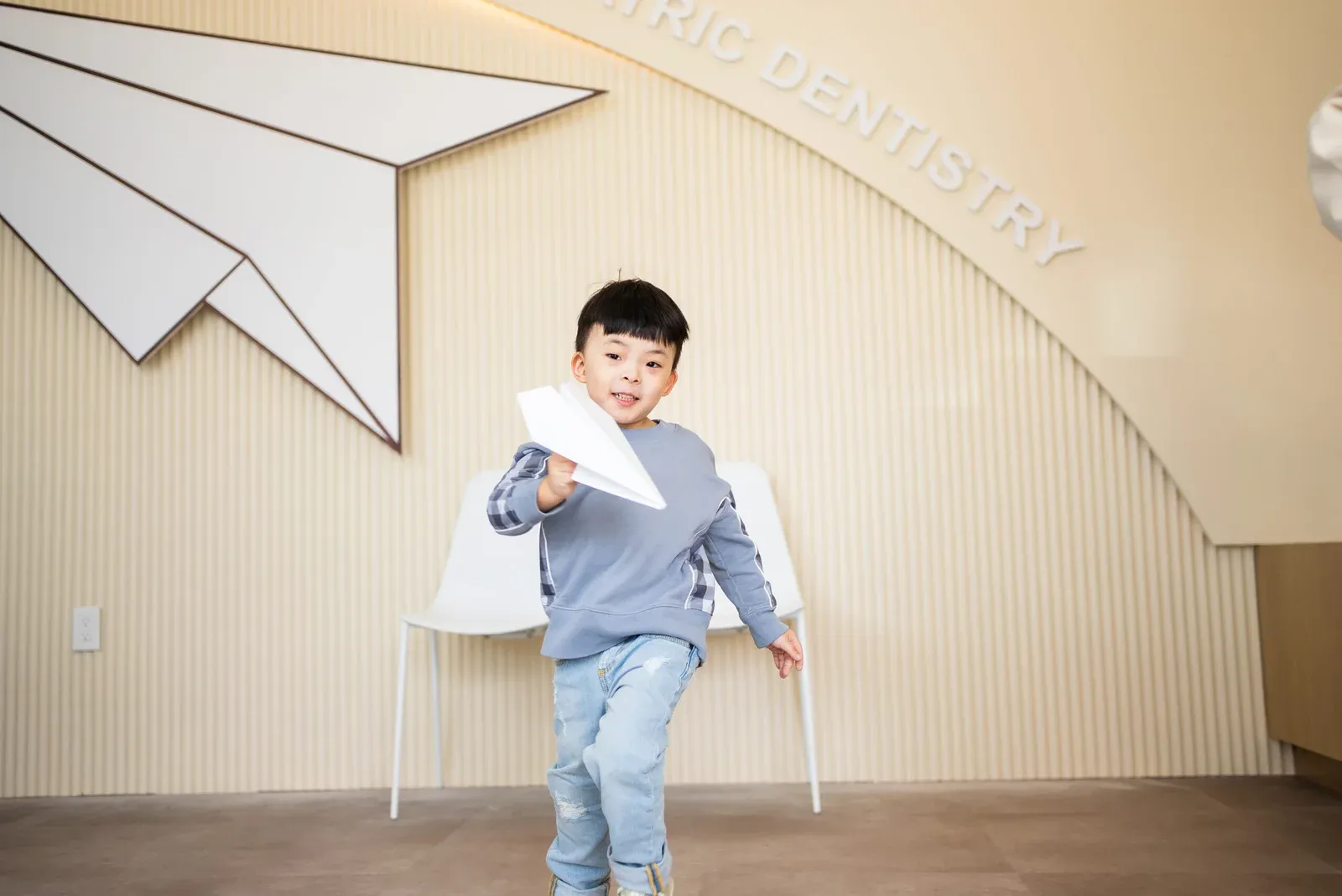Happy child playing with the paper plane, emphasizing the fun, comfort, and stress-free pediatric dental visits.