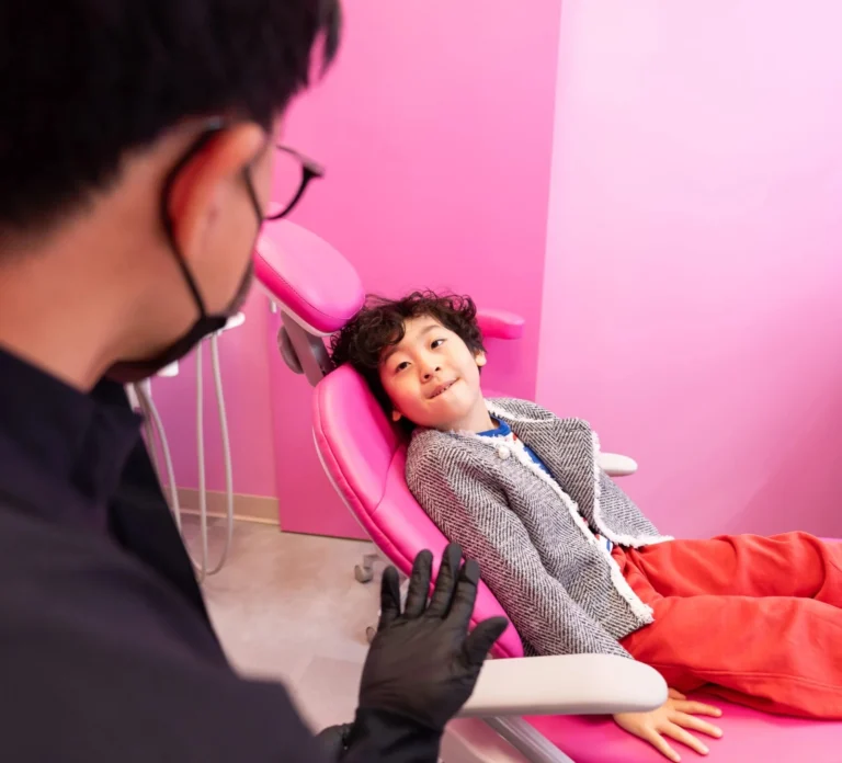 Young boy comfortably reclined in a pink dental chair smiling at Dr. Christopher Pae during his visit